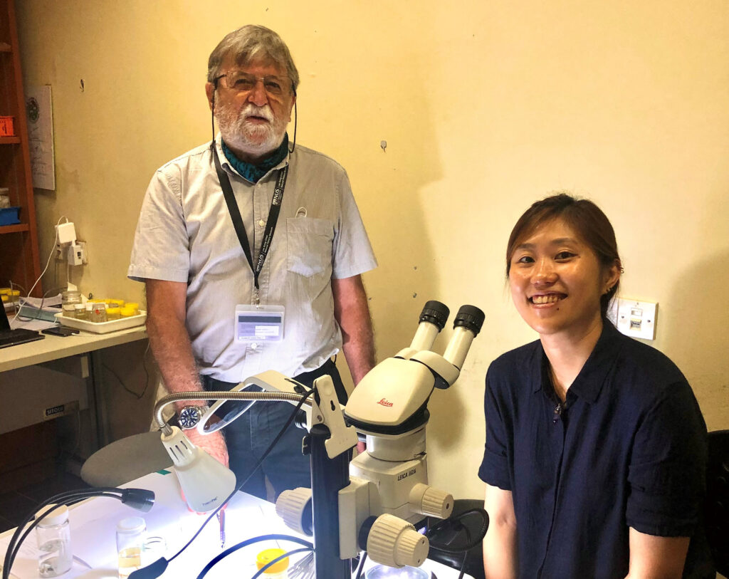 A photograph of Dr Lee on the right, seated behind a microscope, with Dr Richer de Forges standing on the left. 