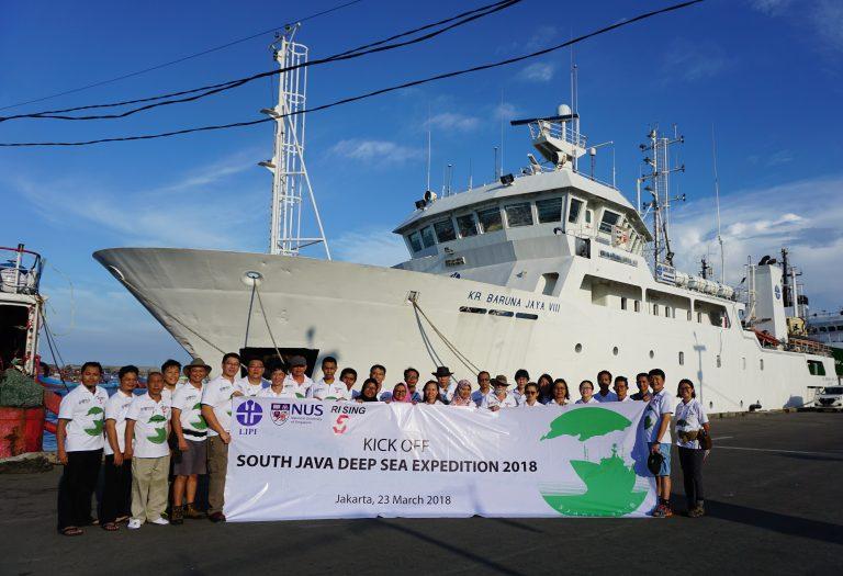 A group photo of the South Java Deep Sea Expedition 2018 team holding a banner and standing in front of the Indonesian research vessel, Baruna Jaya VIII.